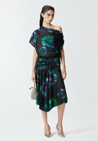 Crna haljina s ljubičastim i zelenim cvjetnim uzorcima, drapirana dizajn s jednim ramenom, nabran struk, lepršava suknja, uparen s metalik srebrnim cipelama.