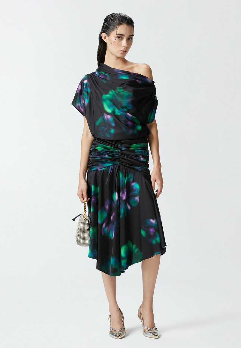 Crna haljina s ljubičastim i zelenim cvjetnim uzorcima, drapirana dizajn s jednim ramenom, nabran struk, lepršava suknja, uparen s metalik srebrnim cipelama.