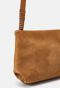 Brun ruskind skuldertaske med tekstureret overflade. Den justerbare rem har et stribet design, der fremhæver dens moderne udseende.