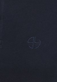 Navyblaues Baumwollgewebe mit einem dezenten gestickten Logo in einer dunkleren Nuance. Glatte Textur mit einem klaren, minimalistischen Design.