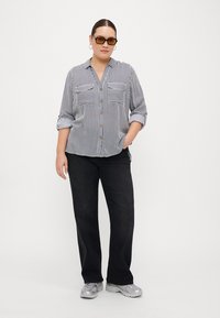 Chemise rayée à boutons avec deux poches poitrine ; associée à un pantalon large noir et des baskets grises. Des lunettes de soleil complètent le look.