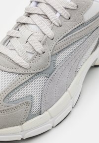 Scarpa sportiva grigia realizzata in materiali a rete e suede, con accenti testurizzati, lacci piatti e suola bianca imbottita.
