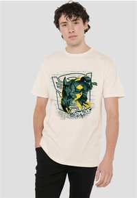 Cream-colored cotton t-shirt featuring a graphic of a black and yellow robotic character on the front, with a textured background design.