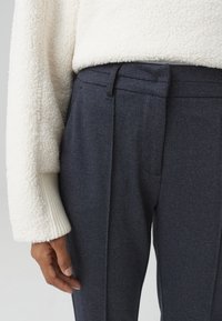 Pantaloni strutturati blu navy con una vestibilità sartoriale, dotati di un davanti piatto e tasche laterali, abbinati a un maglione bianco peloso con polsini a coste.