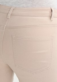 Jeans in denim beige con un design aderente, una trama sottile e tasche posteriori con un singolo dettaglio cucito sui bordi.