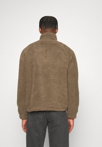 Braune Fleecejacke mit hohem Kragen, weicher Textur und entspannter Passform. Verfügt über elastische Bündchen und Bund, mit schlichtem Design.
