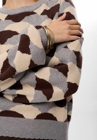 Pull en tricot présentant un motif abstrait beige, gris et marron. Fini avec des poignets gris côtelés et un ourlet festonné.