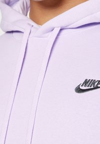 Ljuslila hoodie av mjukt tyg, med en svart broderad Nike-logotyp på bröstet och dragsnören. Mjuk textur och enkel design.