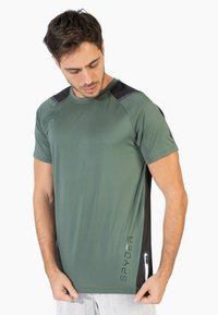 Camiseta deportiva verde con acentos negros en los hombros, mangas cortas y corte ajustado. Logo "SPYDER" en la parte inferior izquierda. Textura de tela suave.