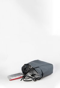 Grå syntetisk taske med en flad rektangulær bund, justerbare sorte stropper og et ternet interiør. Indeholder en lille sølvpung med en rød lynlås.