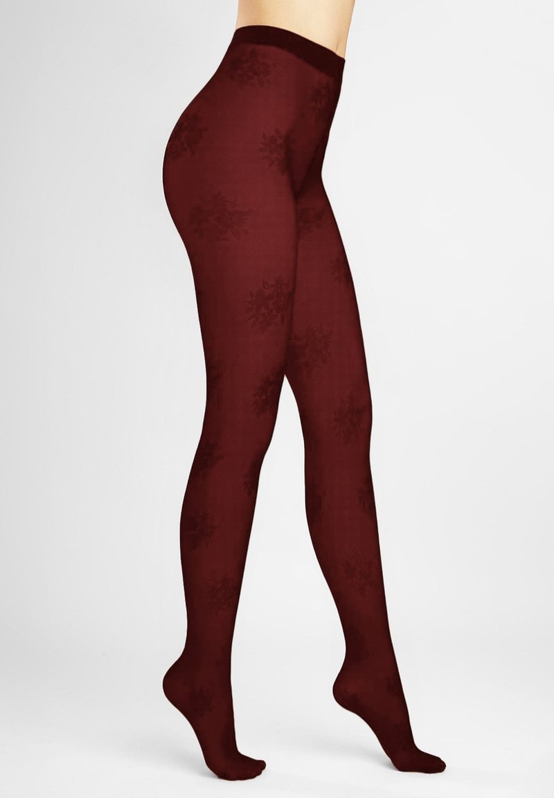 Damskie nogi w bordowych przezroczystych rajstopach z delikatnym wzorem płatków śniegu, stojące na palcach na jednolitym białym tle.