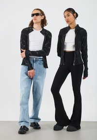 Sorte mønstrede jakker, hvide crop tops, lyseblå løse jeans, sorte flagrende bukser og kraftige sorte sko båret af to modeller mod en lys baggrund.