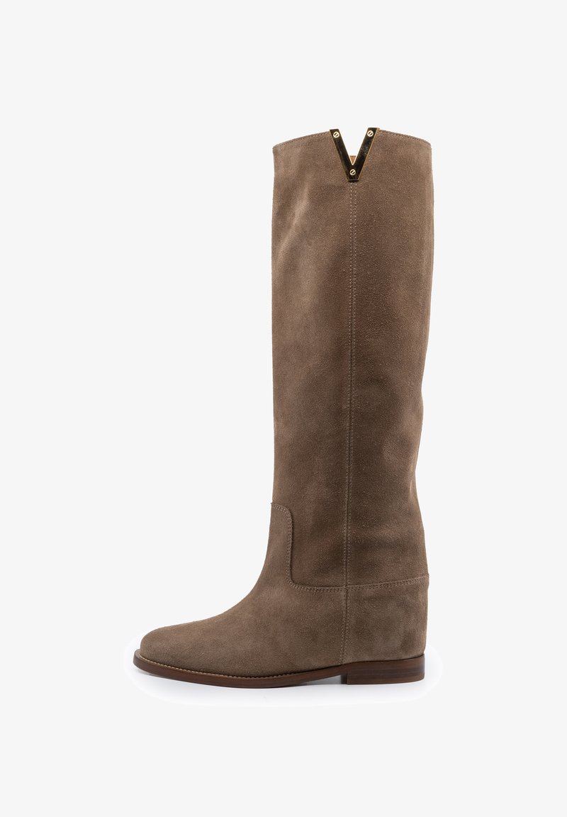 Botte haute en daim marron avec un petit talon compensé et un accent en métal doré en forme de V au bord supérieur.