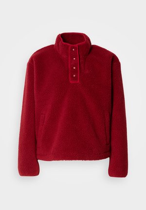 Czerwony polarowy sweter z wysokim kołnierzem, listwą na guziki i dwiema bocznymi kieszeniami; miękki, teksturowany materiał i luźny krój.