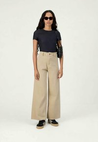 Marineblå tætsiddende t-shirt parret med beige vidde bukser, sorte solbriller og sort taske. Bukserne har høj talje og en glat tekstur.