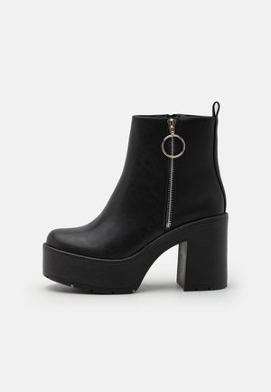 Sort læder platform ankle støvle med chunky høj hæl, sølv side lynlås og rund trækflap på ensartet lyse baggrund.