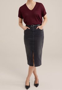 Bordeaux gebreide V-hals top met zigzagpatroon, gecombineerd met een hoge taille zwarte denim kokerrok met een split aan de voorkant. Zwarte puntige hakken.