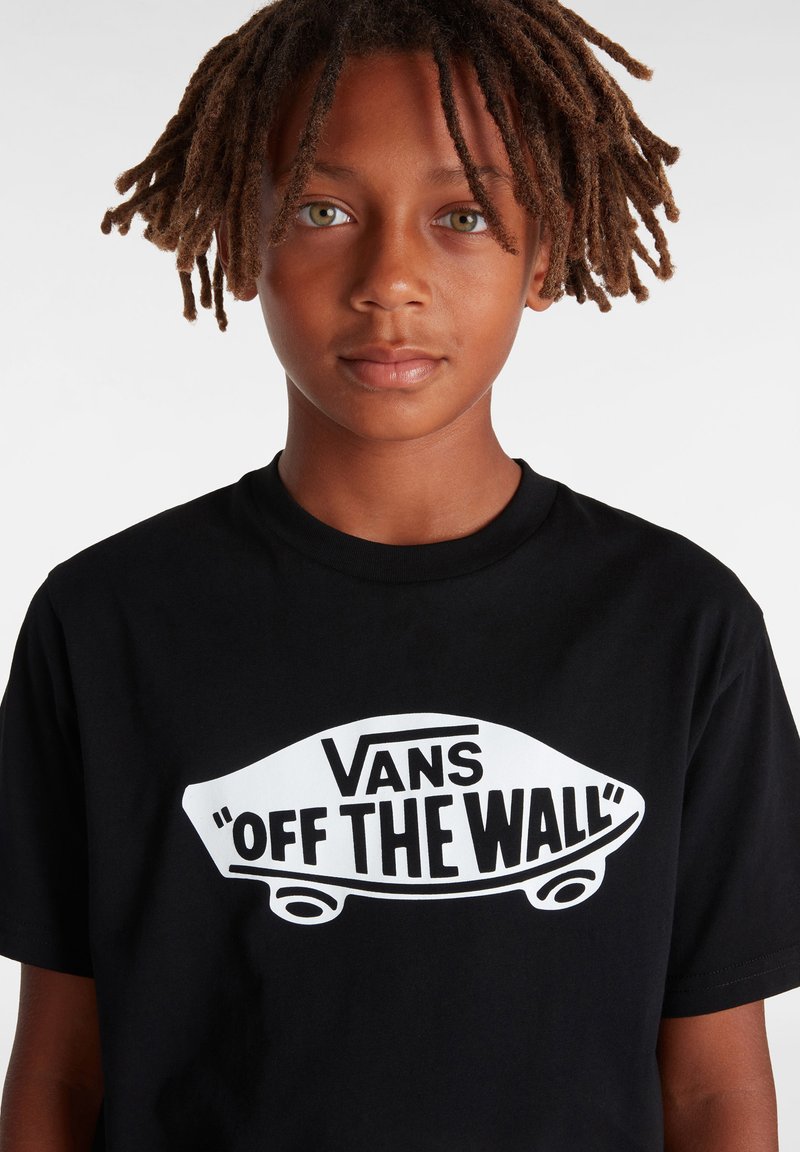 Camiseta de algodón negra con un gran logo blanco "Vans 'OFF THE WALL'" y un gráfico de patineta en el centro. Mangas cortas y escote redondo.