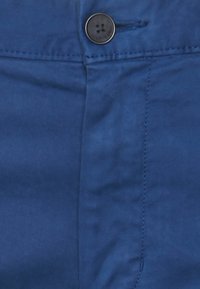 Blå byxfabric med en närbild av en svart knapp och sydda sömmar nära midjan.