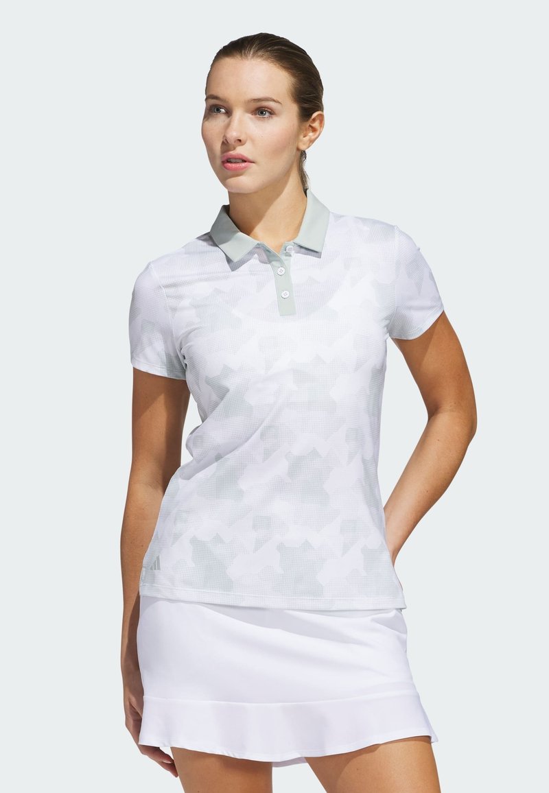 Hvid polo-shirt med et subtilt geometrisk mønster, lysegrå krave, korte ærmer og knaplukning; parret med en hvid nederdel.