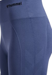 Close-up af blå teksturerede atletiske leggings med ribmønstre og sort "hummel" logo på taljen.