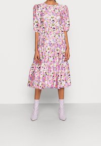 Květinové midi šaty v odstínech růžové, fialové a žluté. Mají balónové rukávy, kulatý výstřih a vrstvené volány na spodním lemu.