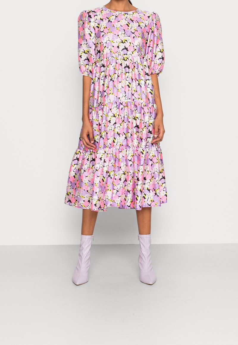 Květinové midi šaty v odstínech růžové, fialové a žluté. Mají balónové rukávy, kulatý výstřih a vrstvené volány na spodním lemu.