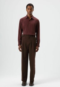 Bordeauxrode blouse met lange mouwen en subtiele glans, met knoopsluiting aan de voorkant, gecombineerd met hooggetailleerde bruine pantalon, beide in getailleerde pasvorm.