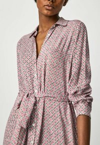 Robe à motifs roses avec des motifs floraux, devant à boutons, manches longues et ceinture à nouer. Tissu doux et texturé avec une coupe décontractée.