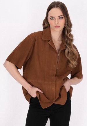 Bruine suède shirt met korte mouwen, een notch-kraag en drukknopen aan de voorkant. Voorzien van zijzakken en een ontspannen silhouet.