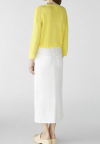 Gelber Strickpullover mit langen Ärmeln und einem cropped Design, kombiniert mit einem langen weißen Jeansrock und beigen Plateausandalen.