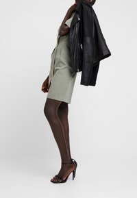 Olive green shirt dress with a button front and short sleeves, paired with black leather jacket and black strappy high heels. Smooth texture.