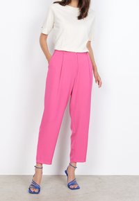 Pantalons taille haute roses avec des plis, offrant une coupe ample. Associés à un haut crème à manches courtes et des sandales bleues à brides.