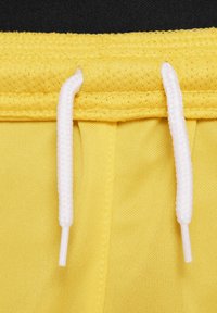 Gele sportshorts met witte trekkoorden, met een mesh-textuur en een gelaagde tailleband, close-up van de stof en de touwen.