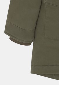 Olivově zelená bunda s rukávem a jemně stočeným lemem, prošitými švy a detailním záběrem texturované látky. Design má pohodlný střih.