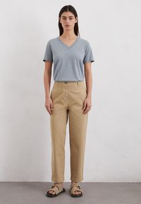 Lichtgrijze v-hals t-shirt, beige rechte pantalon en bruine sandalen met banden. Eenvoudig ontwerp, zachte textuur en een relaxte pasvorm.