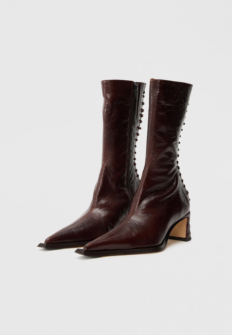 Bruine leren enkellaarzen met puntige neuzen, ritssluiting en decoratieve studs langs de zijkant. Lage schuine hakken en een gladde afwerking.