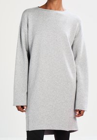 Sudadera gris de gran tamaño, con cuello redondo, mangas largas, textura suave, aberturas laterales en el dobladillo, diseño casual adecuado para superponer.