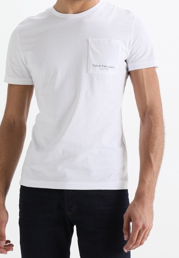 Vit bomull t-shirt med korta ärmar, rundhalsringning och en vänster bröstficka med "Calvin Klein Jeans" logotyp i svart text.