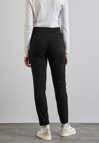 Pantalones negros ajustados hechos de una tela suave, con dos bolsillos traseros y una cinturilla elástica lisa. Combinados con zapatillas blancas y crema.