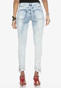 Jasnoniebieskie dżinsowe skinny jeans z postrzępionym dołem, ozdobione srebrnymi ćwiekami, z pięcioma kieszeniami.