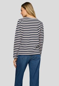 Navy and cream striped long-sleeve shirt with a round neckline, relaxed fit, and soft cotton fabric, paired with blue wide-leg jeans.