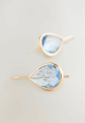 Gold teardrop earrings with faceted light blue stones. Smooth metal and transparent stone details create a delicate, elegant design.