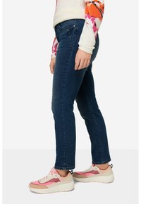 Námořnické modré džíny s úzkým střihem a standardním pětikapsovým designem. Spárovány s růžovými a béžovými teniskami s texturovaným svrškem.