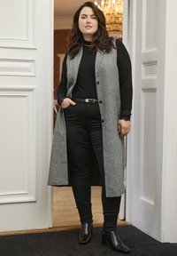 Dugi sivi kardigan s gumbima preko crnogrol majice s visokim ovratnikom, uparen s crnim uskim hlačama i čizmama na visoku petu. Složen dizajn čipke na rukavima.