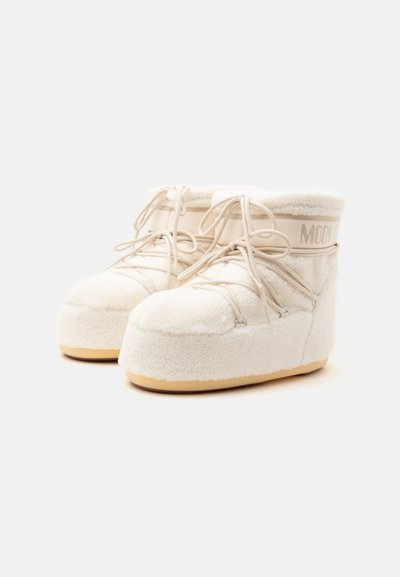 Paire de bottes d'hiver crème à tige haute avec une épaisse doublure en polaire, bouts arrondis, semelles beiges et détails de laçage croisés.