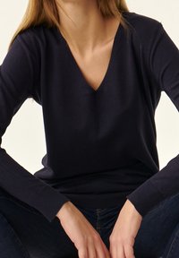 Marineblauer, gestrickter Pullover mit V-Ausschnitt, langen Ärmeln und gerippten Bündchen. Weiche Textur, figurbetonte Silhouette und minimalistische Stilmerkmale.