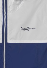 Námořnická a bílá zipová bunda vyrobená z hladkého, lehkého materiálu. Obsahuje vertikální zip a logo "Pepe Jeans" v kursive.