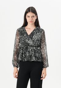 Blusa nera a fiori con maniche lunghe e trasparenti, scollatura a V e orlo a peplum. Presenta delicati motivi floreali bianchi in tutto il capo.