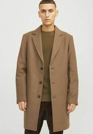Manteau en mélange de laine brun avec des revers crantés, fermeture à cinq boutons et poches latérales, porté par-dessus un pull vert texturé.